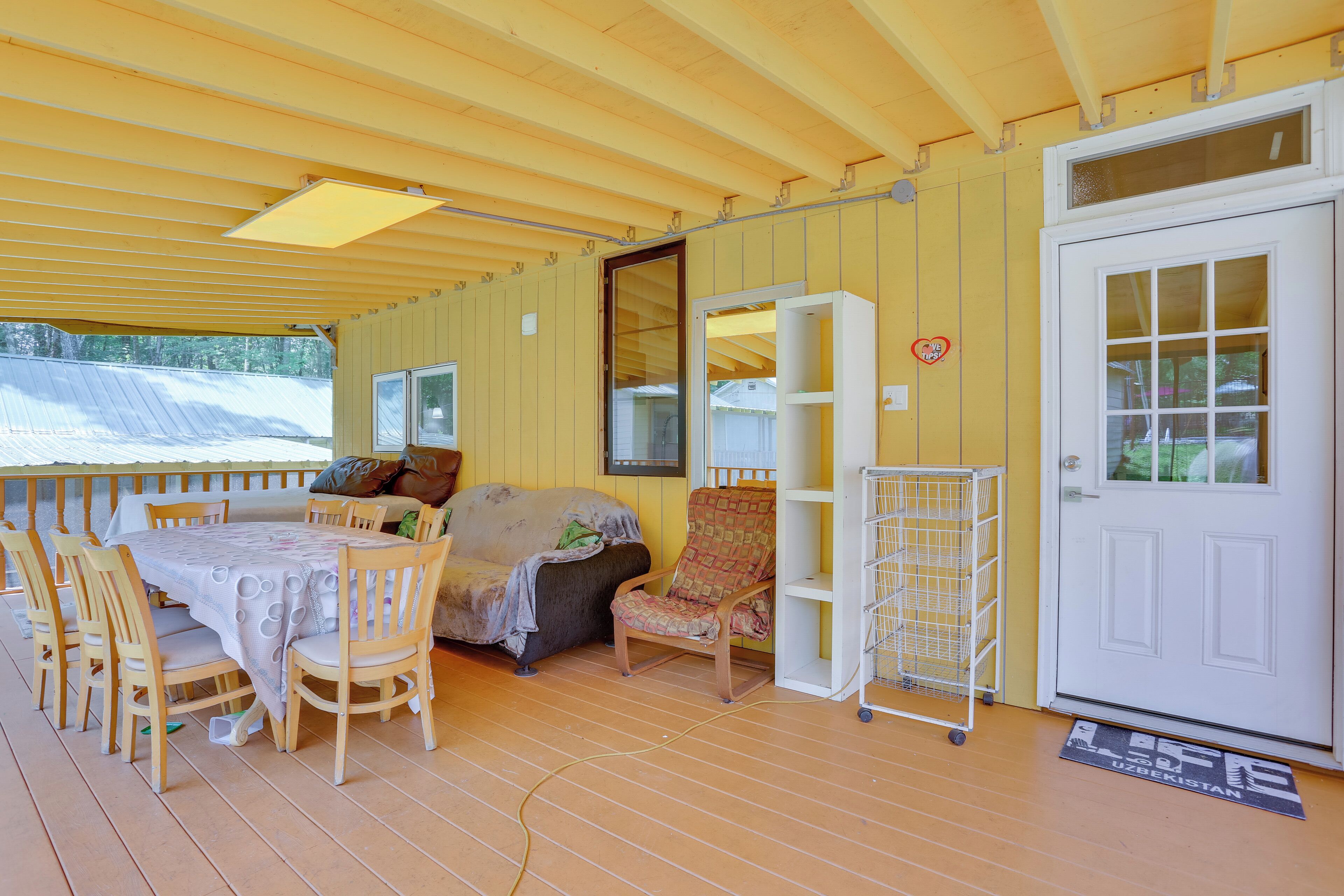A covered porch with a dining table and chairs, a sofa, a chair, a bookshelf, and a door.