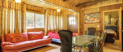 A wooden interior with a glass dining table, leather sofa, and a painting on the wall.