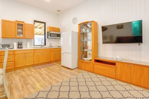 Een keuken met houten kastjes, een magnetron, een koelkast, een klok en een flatscreen tv aan de muur.