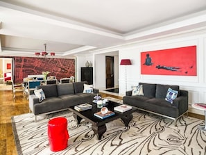 A modern living room with two sofas, a coffee table, and a red accent chair. There is a large red painting on the wall and a map on the opposite wall.