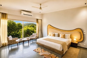 A hotel room with a large bed, a sitting area with a table, and a view of greenery outside. - Alaya Stays Raj Suites Pet-Friendly (Udaipur)
