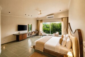 A modern hotel room with a large bed, a desk, a TV, and a view of greenery. - Alaya Stays Raj Suites Pet-Friendly (Udaipur)