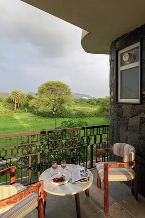 Un balcón con una mesa para dos, una silla y vistas a un paisaje verde con árboles y colinas.