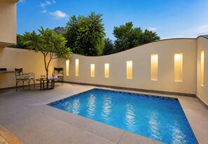 A swimming pool with a tiled deck, a seating area with chairs and a table, and a wall with illuminated panels. - Alaya Stays Raj Suites Pet-Friendly (Udaipur)