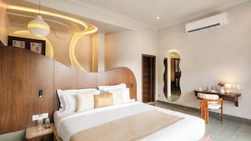 A modern bedroom with a large bed, a wooden headboard, a bedside table, a nightstand, a mirror, a desk with a chair, and an air conditioning unit.