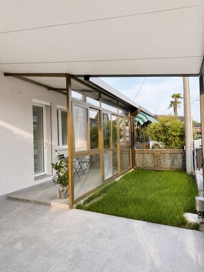 Ein modernes Haus mit einer gläsernen Veranda, einem Rasen und Blick auf die Straße.