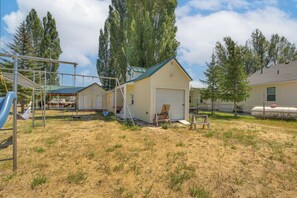 A residential area with a single-story house featuring a garage, a swing set, and a covered patio area. - Bear Lake Cabin w/ Spacious Yard + Patio! (Saint Charles)