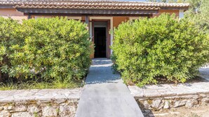 A building with a tiled roof, a stone pathway leading to the entrance, and well-maintained green shrubs on either side. - Zanteva-Psophis cottage (Zakynthos)