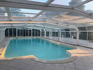Una piscina techada con techo de vidrio, rodeada por un área de patio.