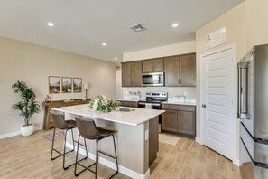 A modern kitchen with a central island, stainless steel appliances, and a dining area with bar stools. - Superstition Mtn Views: Seasonal Golf Getaway (Gold Canyon)