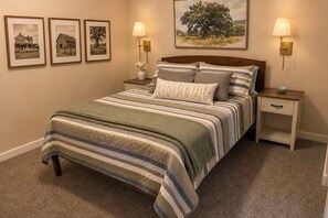 A neatly arranged bedroom with a bed, two bedside tables, a nightstand, a lamp, and framed pictures on the wall.