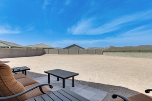 An outdoor patio area with a seating arrangement, including a sofa and a small table, set against a backdrop of a clear sky and distant hills.