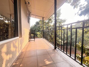 A covered balcony with a tiled floor, metal railing, and a view of greenery. - Unwind Karjat (Khalapur)
