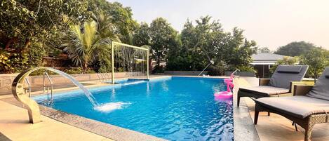 Piscina con fuente de agua, rodeada de sillas de descanso y follaje.