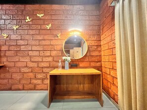 A bathroom with a wooden vanity, a round mirror, and a wall with brick texture and decorative bird motifs. - Unwind Karjat (Khalapur)