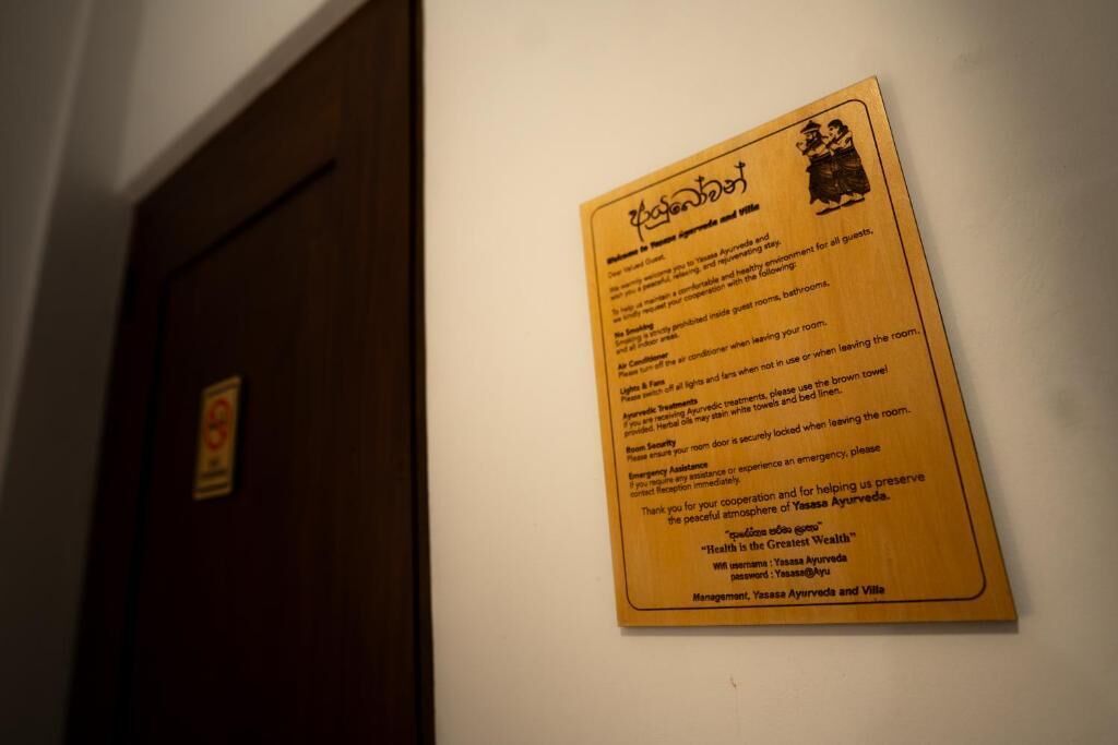 Uma placa de madeira com texto e um logótipo, fixada numa parede num corredor.