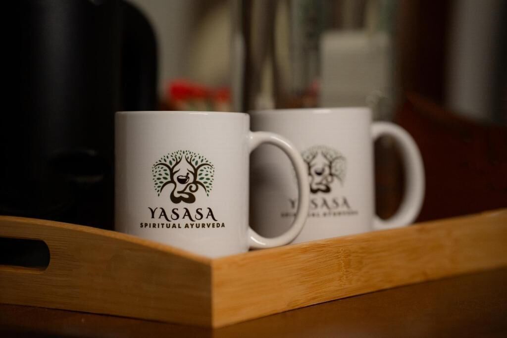 Dos tazas blancas con un logotipo y texto sobre una bandeja de madera.