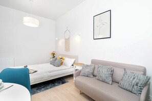 A modern, minimalist bedroom with a bed, a sofa, a bedside table, a hanging macrame decoration, and a framed abstract artwork. - Stylish Apartment Near the Old Market Square | Pet Friendly (Poznań)