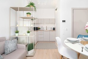 Eine moderne Küche mit weißen Schränken, einem eingebauten Ofen und einer Mikrowelle. Ein Esstisch mit Tellern und Gläsern sowie eine Couch mit Kissen sind ebenfalls vorhanden.