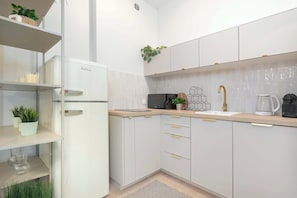 Eine moderne Küche mit weißen Schränken, einer integrierten Mikrowelle, einer Kaffeemaschine und einem Waschbecken mit goldenem Wasserhahn.
