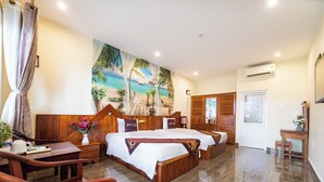Une chambre d’hôtel avec un grand lit, un bureau et une chaise. Il y a un tableau au mur et un appareil de climatisation au plafond.