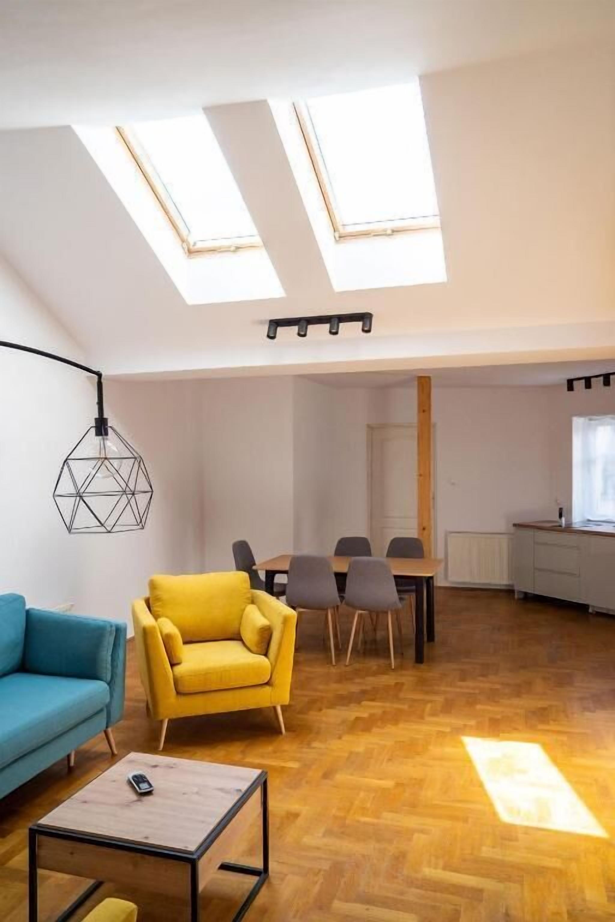 En rummelig stue i loftstil med højt til loftet, ovenlys, et spiseområde og et køkken.