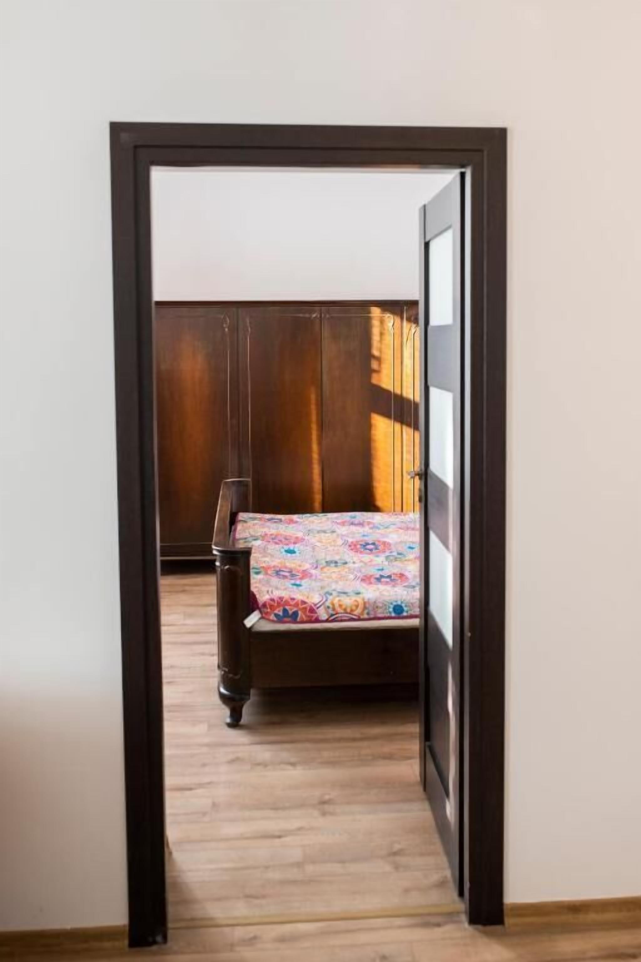 Una puerta que da a un dormitorio con cama, armario de madera y colcha estampada.