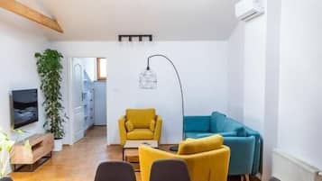 A modern living space with a dining table, chairs, a sofa, and a TV.