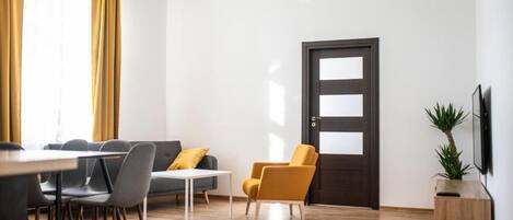 A modern living room with a sofa, chairs, a dining table, and a TV.