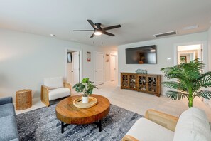 Ein modernes Wohnzimmer mit einem runden Couchtisch, einer Couch, einem Sessel, einem Fernseher und einem Deckenventilator.