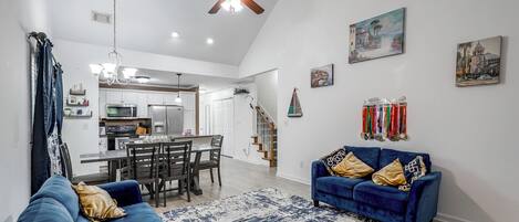 A spacious living room with a blue sofa, a dining area, and a kitchen in the background.