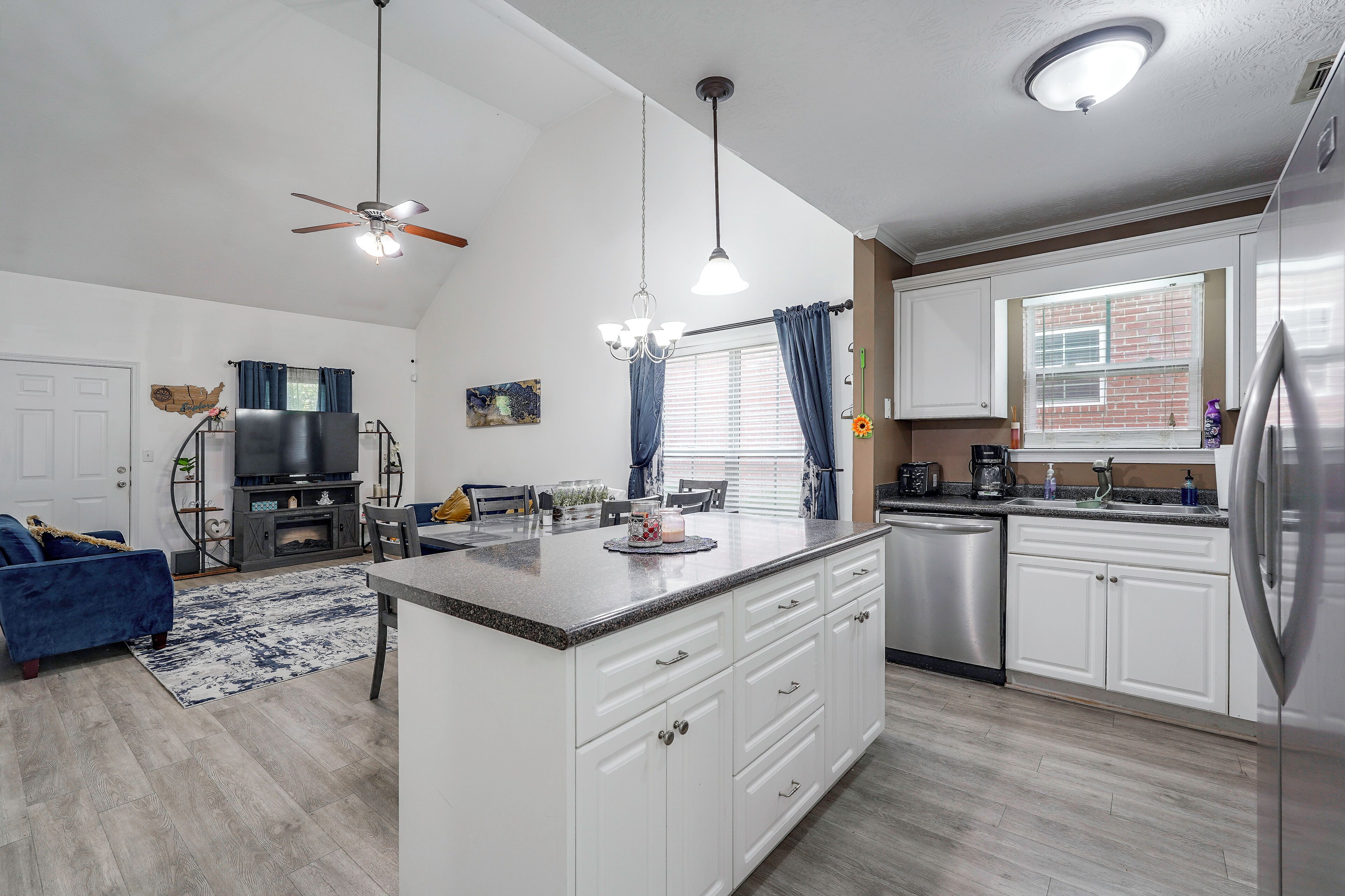 A modern kitchen with white cabinets, a stainless steel refrigerator, and a dining area with a blue sofa and a fireplace.
