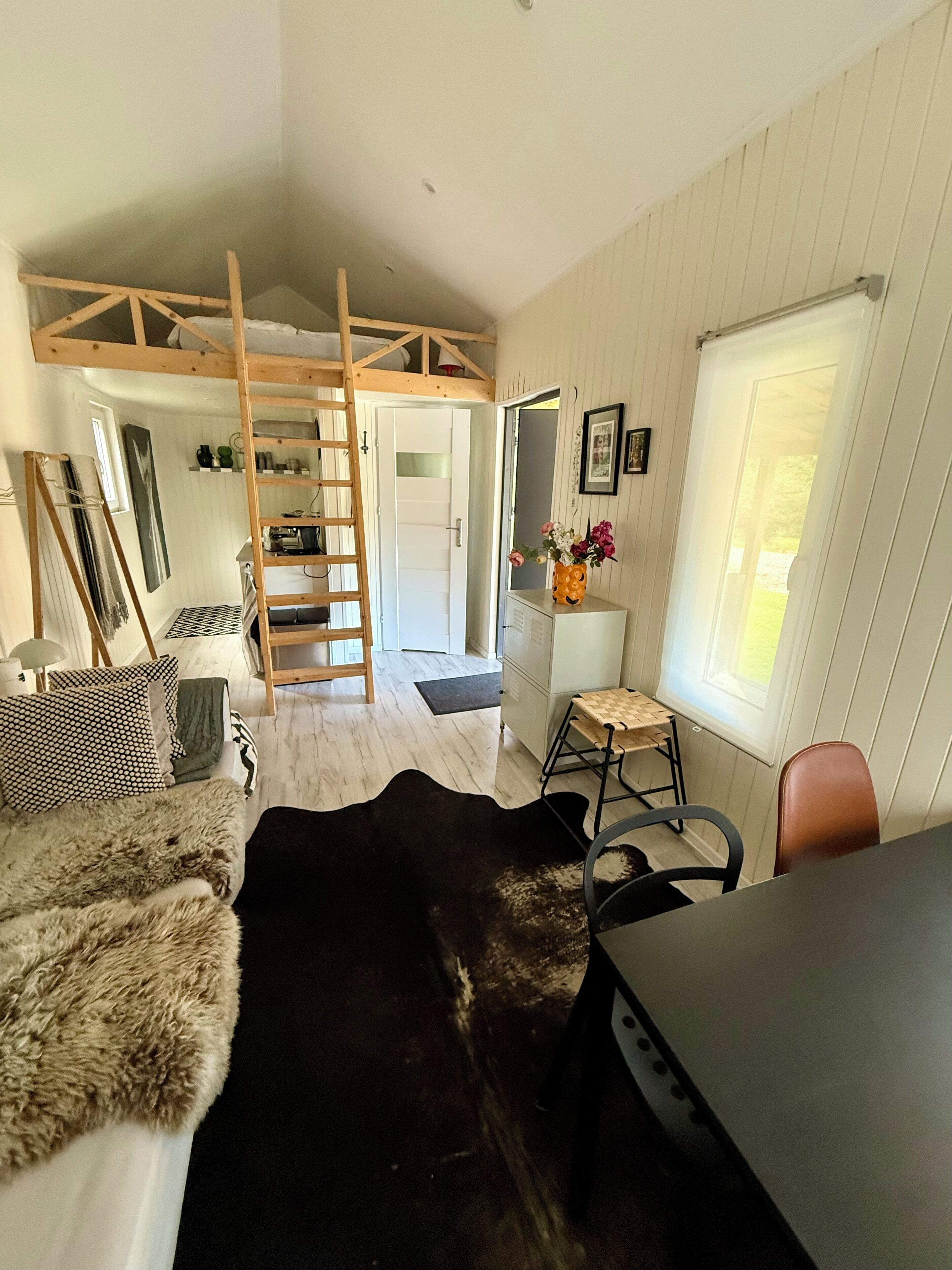 Una habitación con cama de altillo, un escritorio, una silla, una escalera y un ventanal.