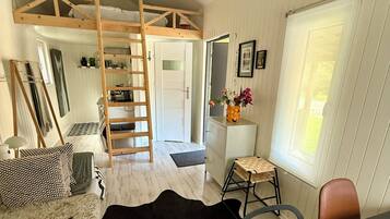 Una habitación con cama de altillo, un escritorio, una silla, una escalera y un ventanal.