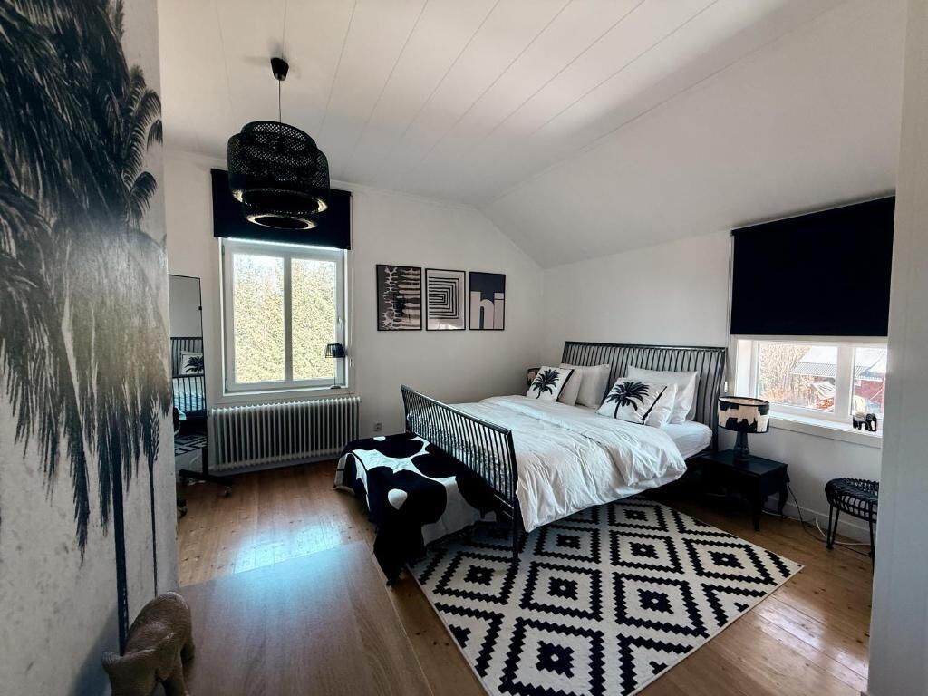 Ein Schlafzimmer mit Bett, Fenster, Heizkörper, Teppich und einer Wand mit einem Gemälde.