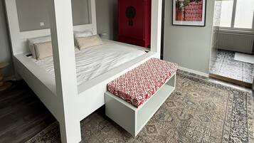 Een slaapkamer met een hemelbed, een rode kast, een kamerkleed met patroon en een ingelijste foto aan de muur.