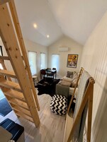 A room with a wooden staircase, a sofa, a dining table with chairs, and a poster on the wall.