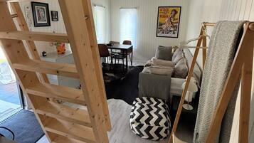 Una habitación con cama tipo altillo, comedor y sala de estar con sofá y alfombra.