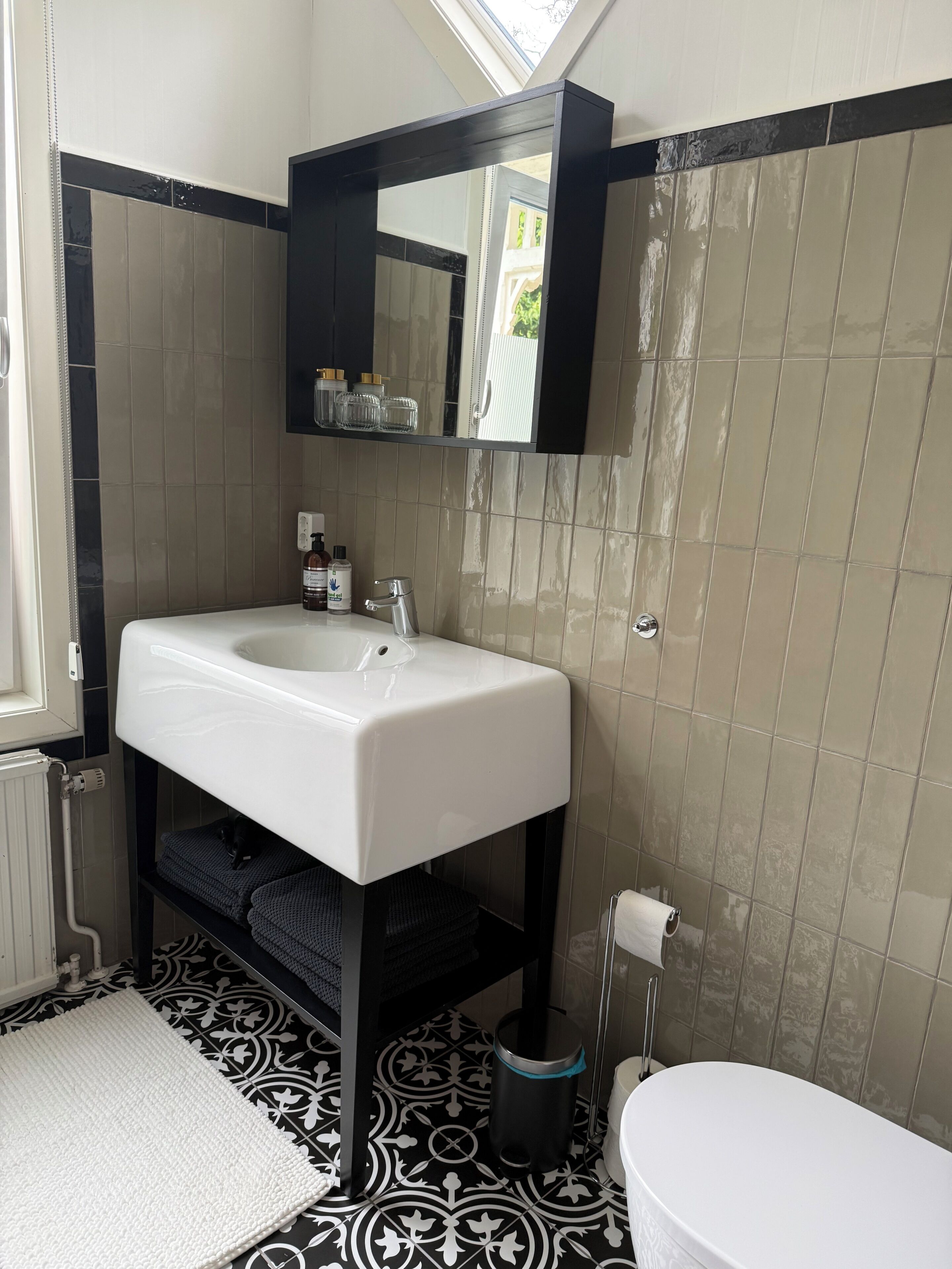 Ein Badezimmer mit einem weißen Waschbecken, einem Spiegel darüber, einer Toilette und fliesenbelagten Bodenfliesen.
