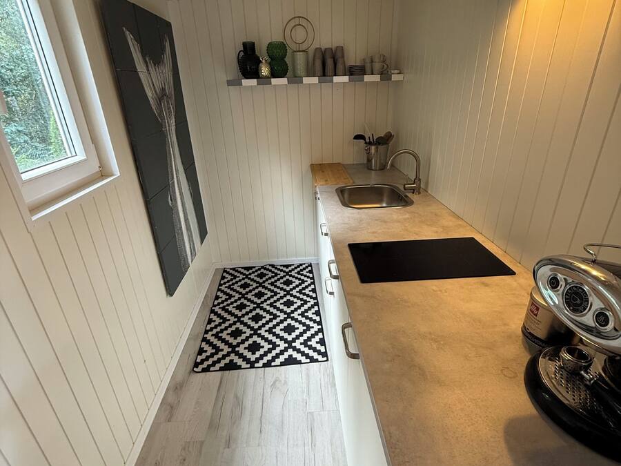 A kitchen with a wooden floor, a black and white patterned rug, a stainless steel sink, and a stove.
