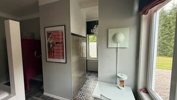 Une chambre d’hôtel moderne avec vue sur l’extérieur, une table blanche avec une lampe, un tapis à motifs et une affiche accrochée au mur.