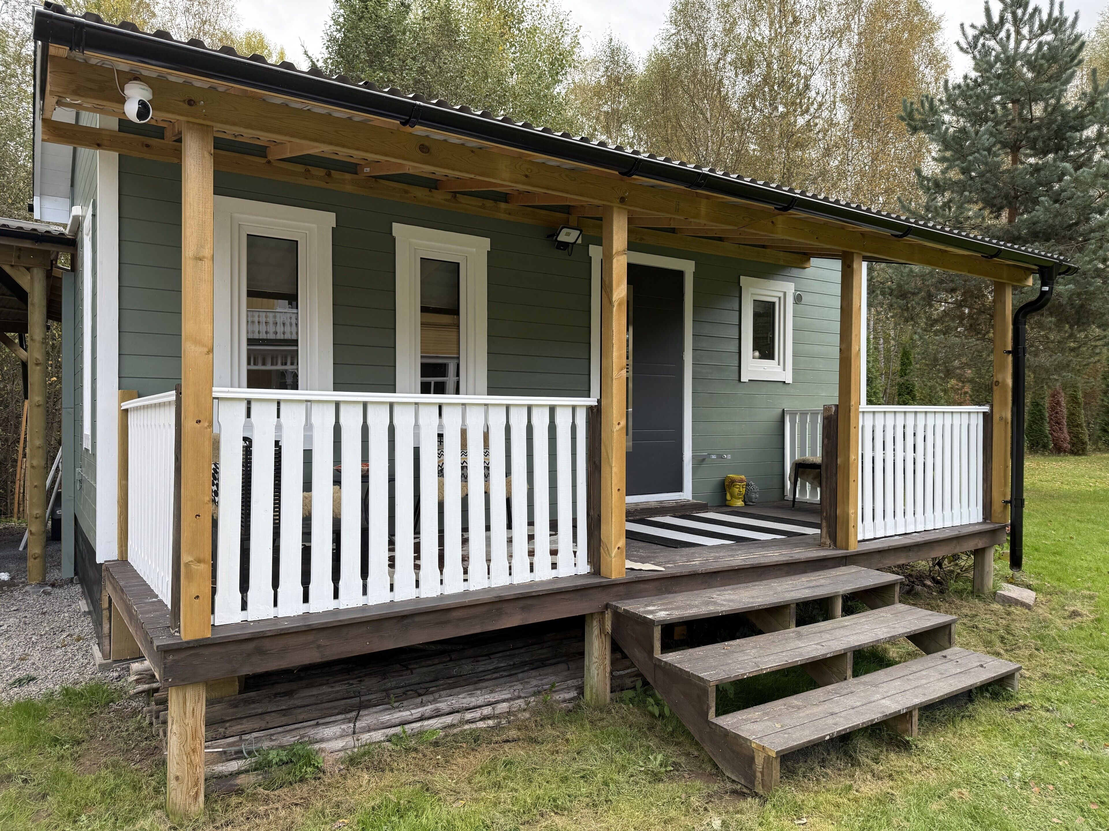 En stuga byggd av trä med en veranda, en ytterdörr och en liten uteplats.