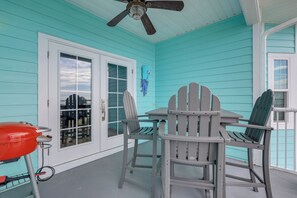 A covered porch with turquoise siding, a ceiling fan, and a table with two Adirondack chairs.