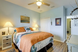 A bedroom with a bed, bedside lamps, a ceiling fan, a door, and a wall with a picture.