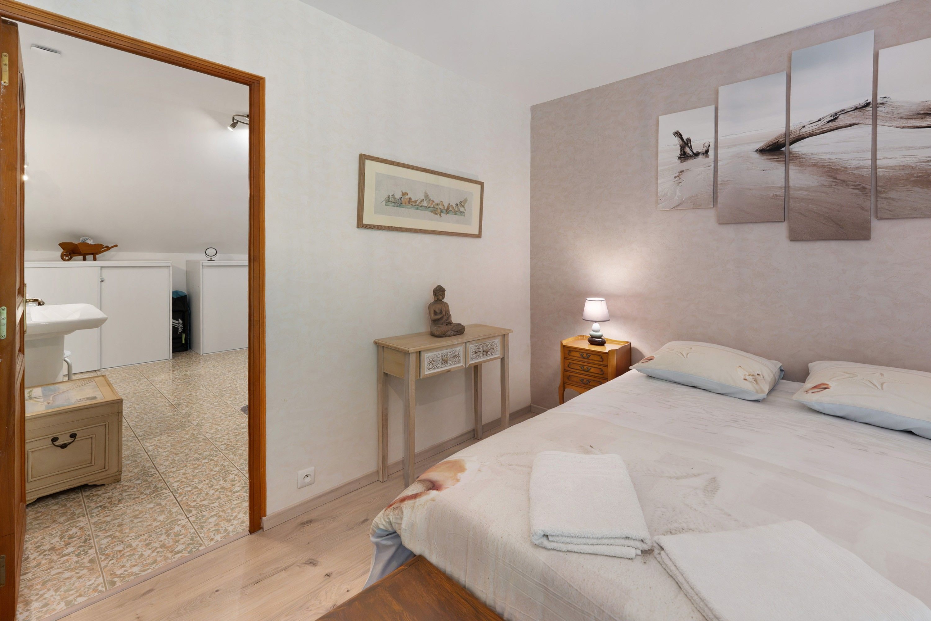 A bedroom with a bed, bedside table, lamp, and a painting on the wall.