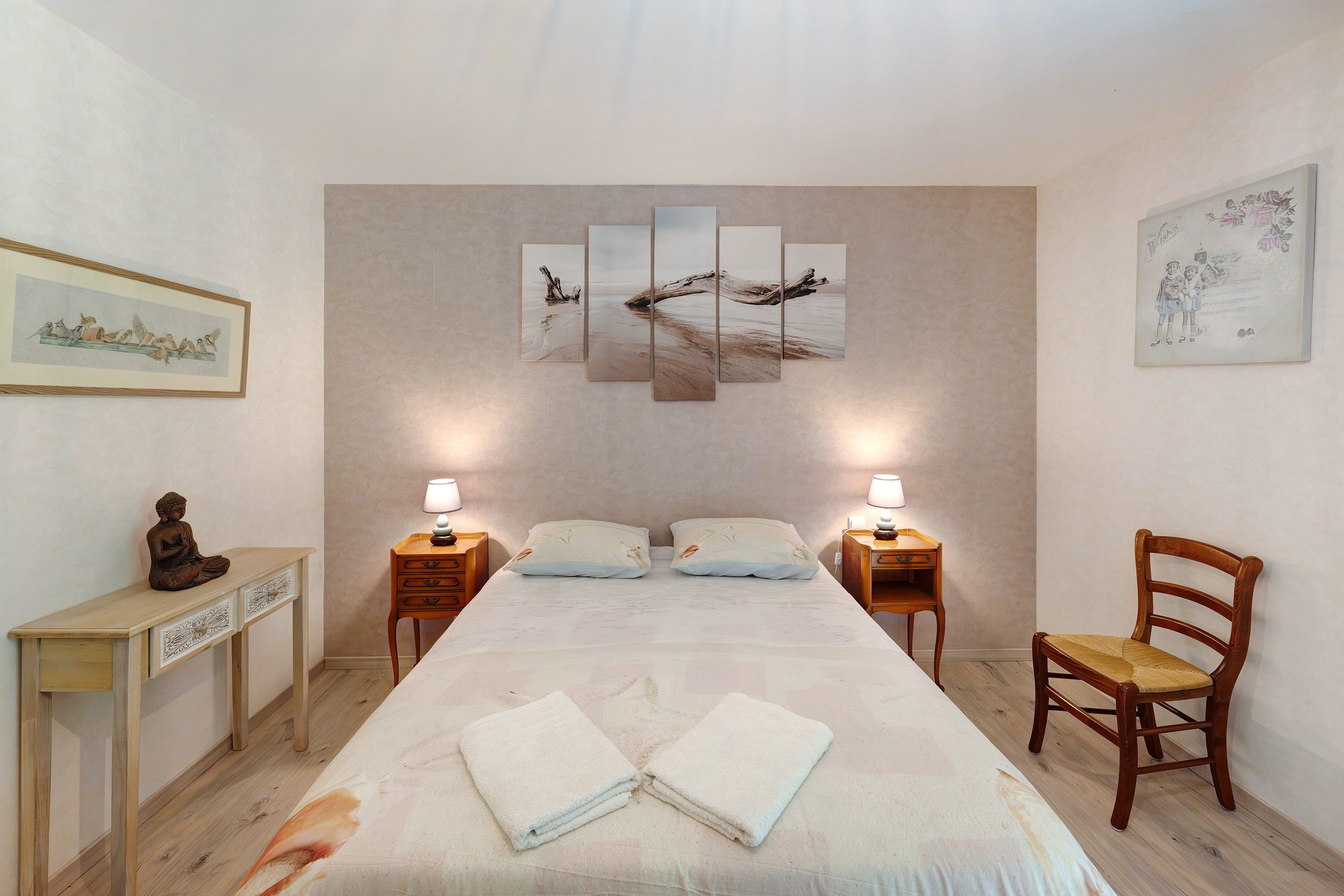 Una camera d'albergo con un letto grande, due comodini, una sedia e opere d'arte alle pareti.