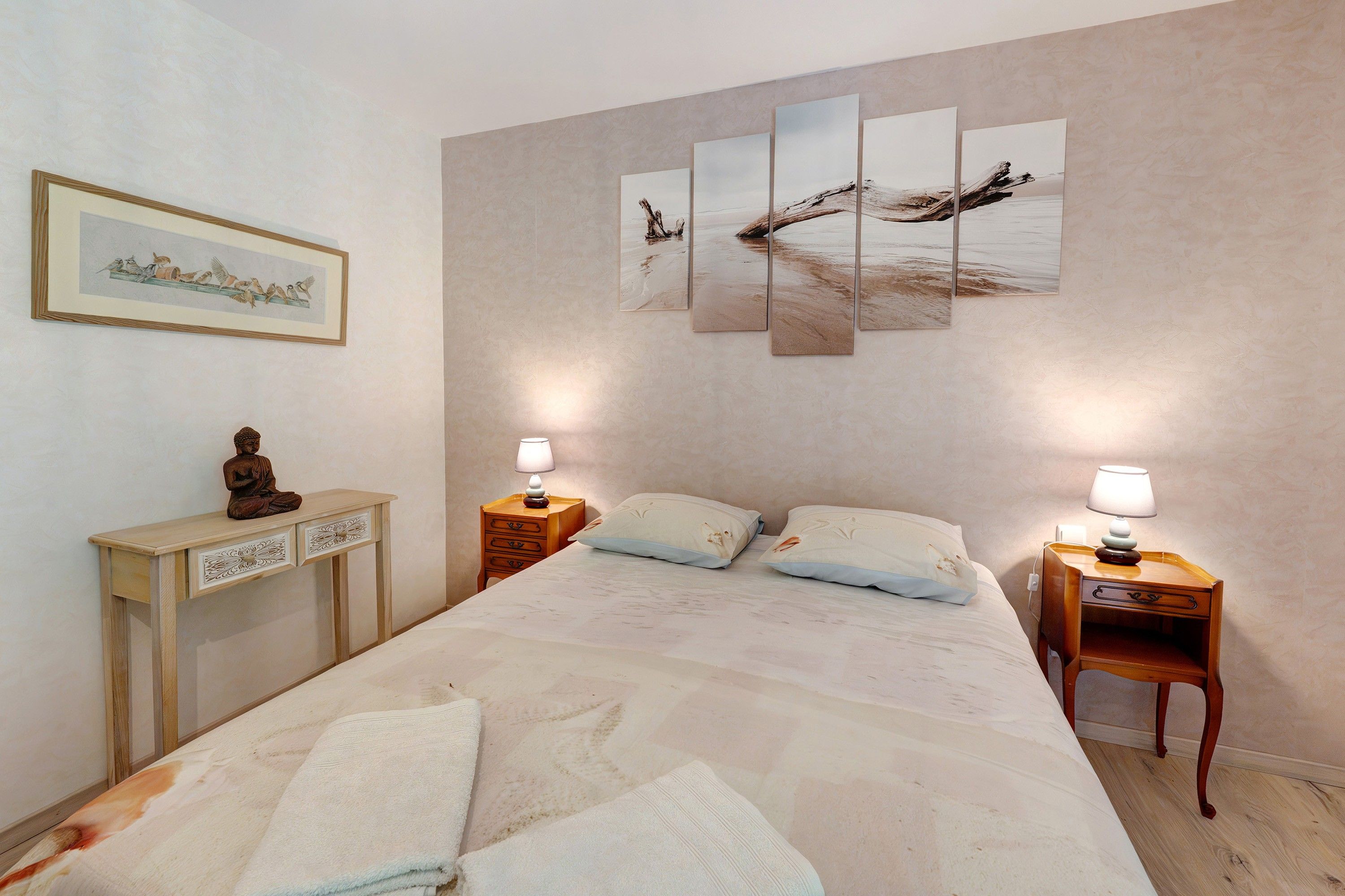 A hotel room with a bed, two bedside tables, a nightstand, a small cabinet, and a wall-mounted painting.