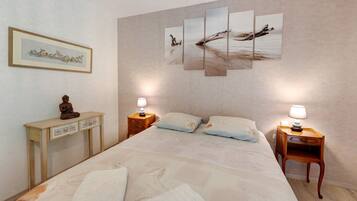 A hotel room with a bed, two bedside tables, a nightstand, a small cabinet, and a wall-mounted painting.