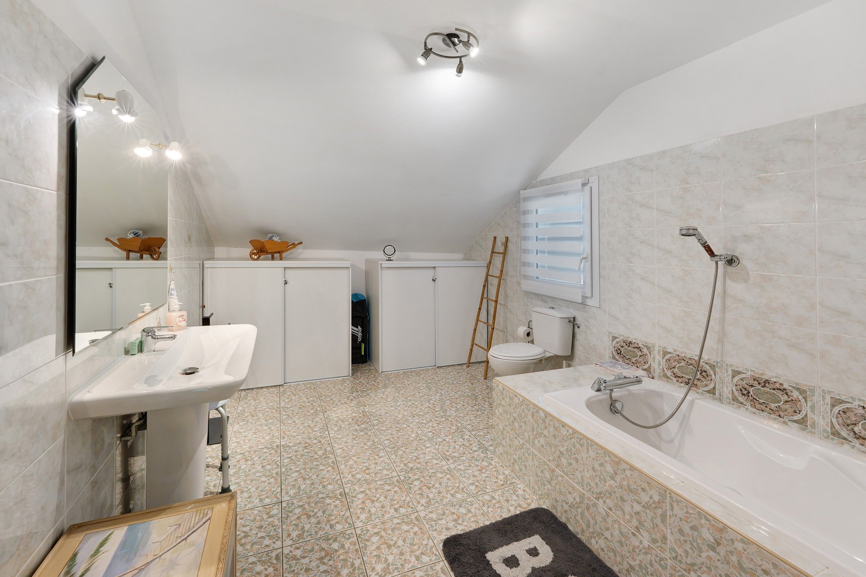 A bathroom with a white sink, mirror, and shower. There are cabinets and a ladder.