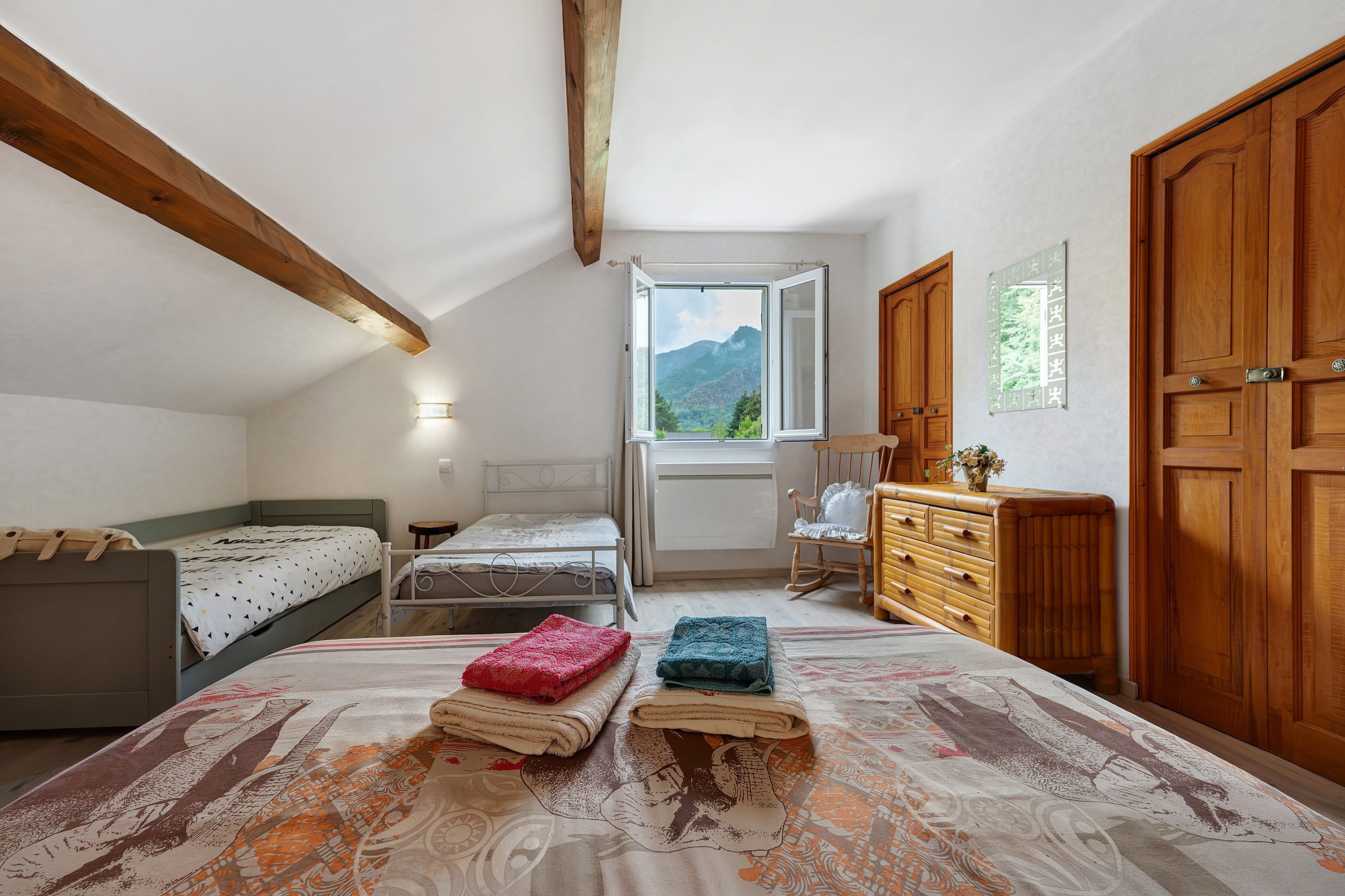A bedroom with a bed, a dresser, a chair, and a window with a view of mountains.